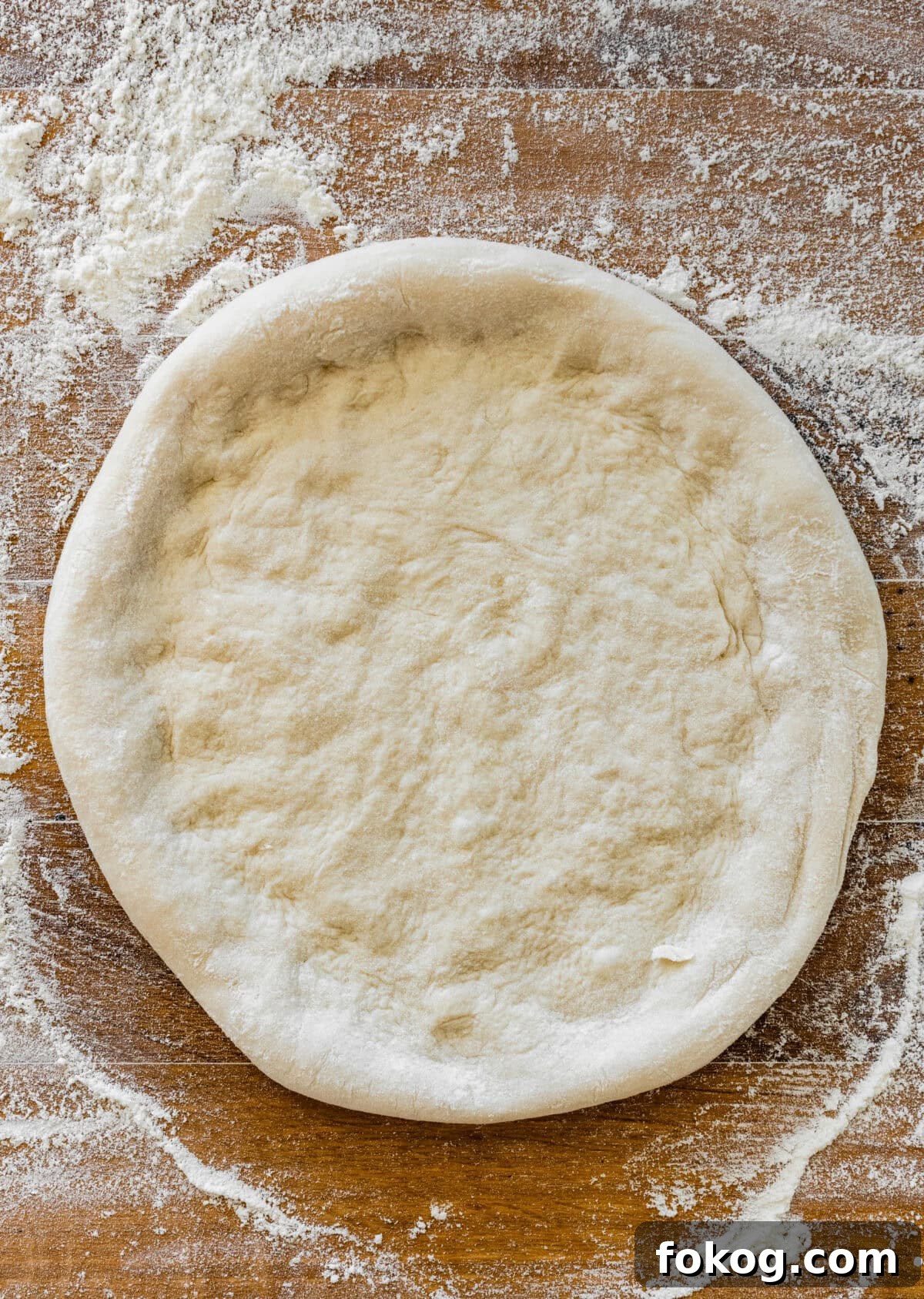 A dough ball rolled out on a wooden surface.