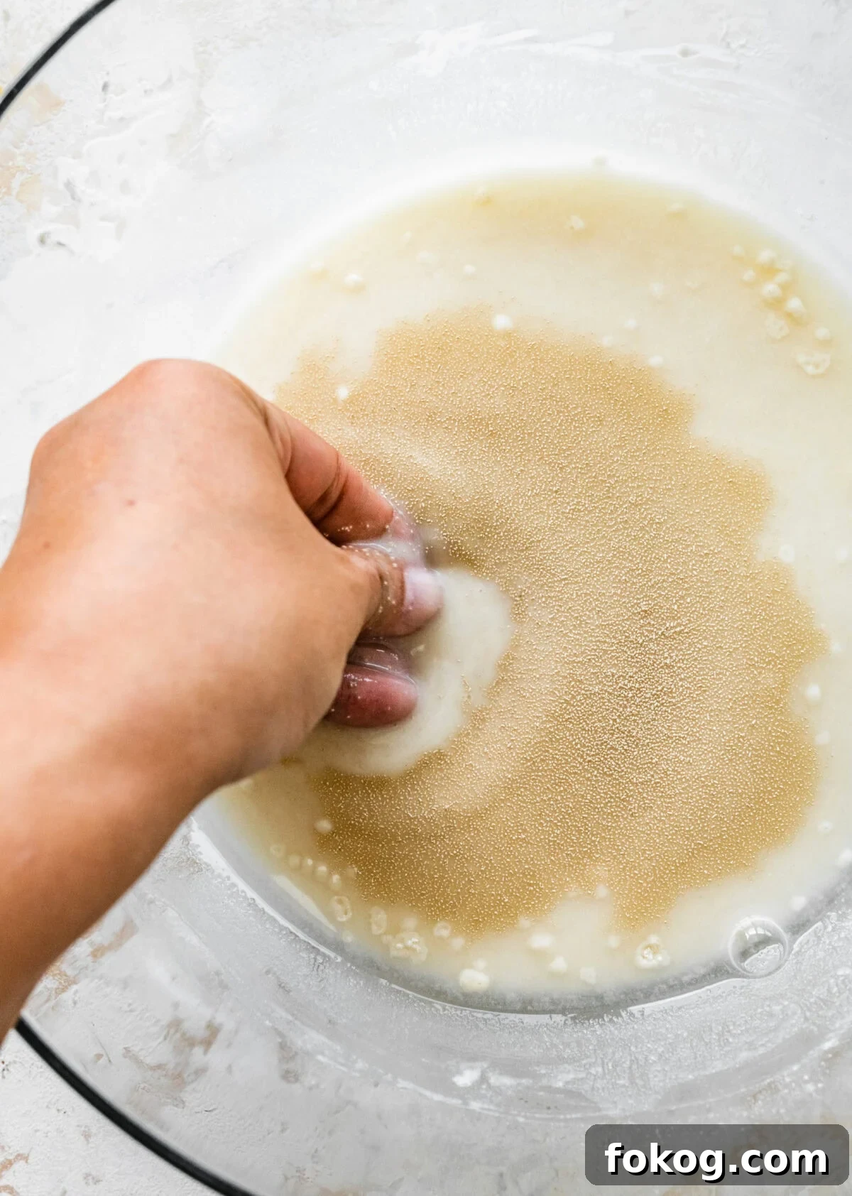 A person's hand is stirring a bowl of yeast and flour with water.