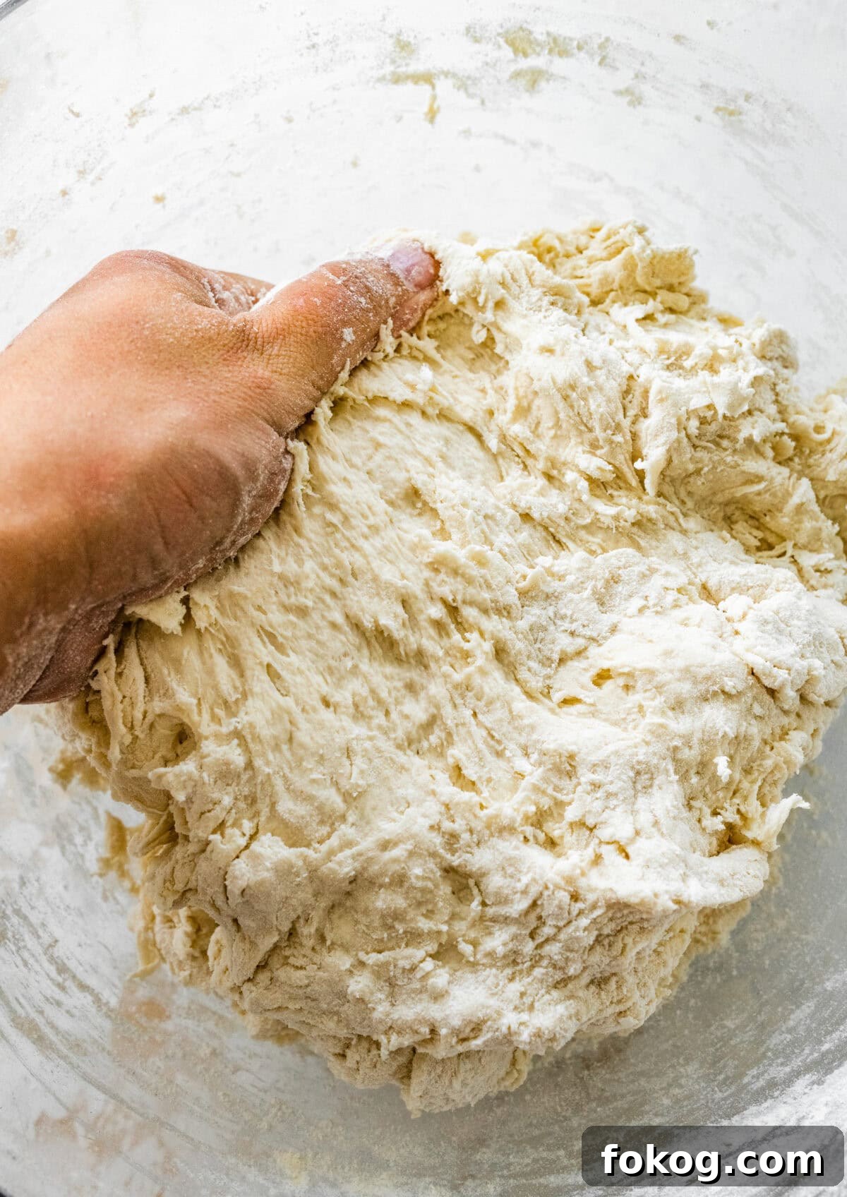 A person's hand is holding a bowl of dough