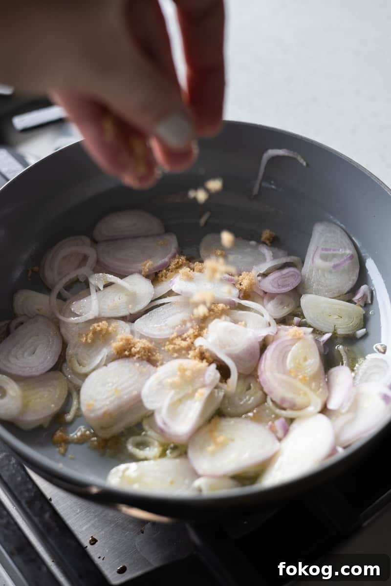 Sliced shallots in a small skillet being sprinkled with brown sugar. 