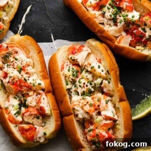 Lobster rolls topped with herbs and spices on a dark slate surface.