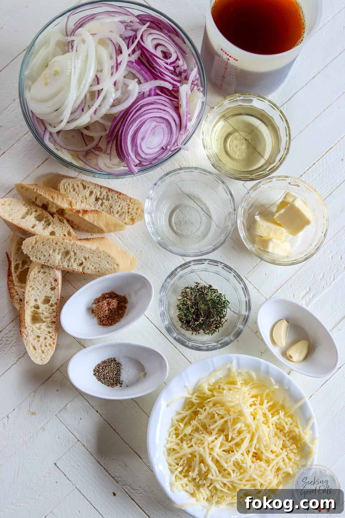 Ingredients needed for making French onion soup on a white wooden board.