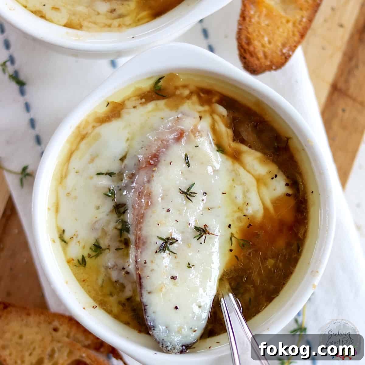 A white bowl of classic French onion soup served in a white bowl with a spoon.