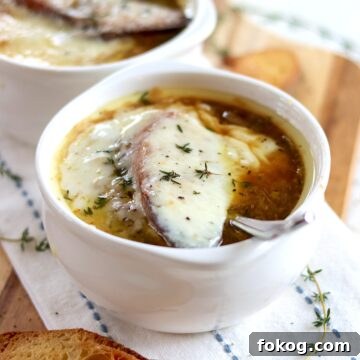 Gooey melted cheese over a crouton floating on French onion soup in a white crockery bowl.