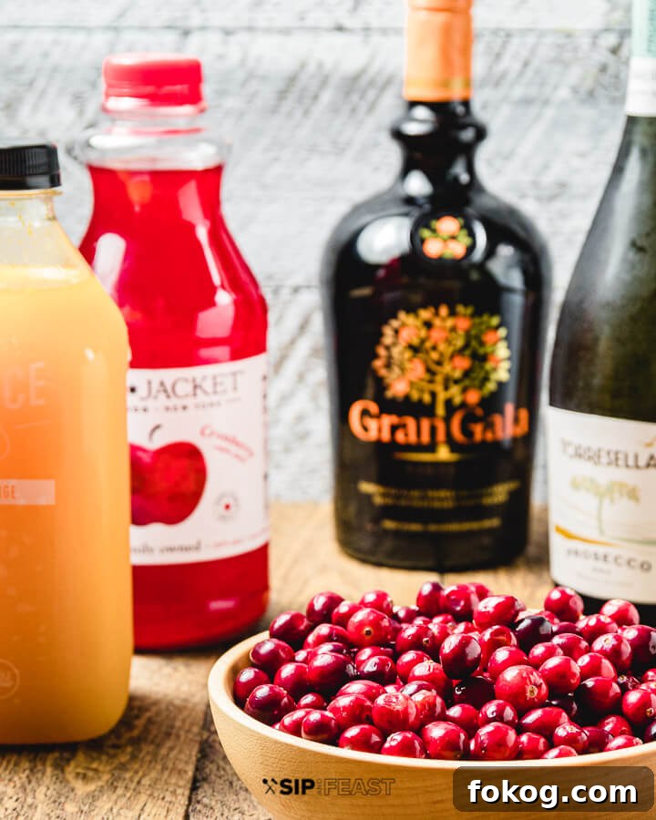 Cranberry Mimosa - sipandfeast.com #cranberrymimosa #holidaydrinks #cocktails Ingredients shown: orange Juice, cranberry juice, Gran Gala, prosecco, and bowl of cranberries.
