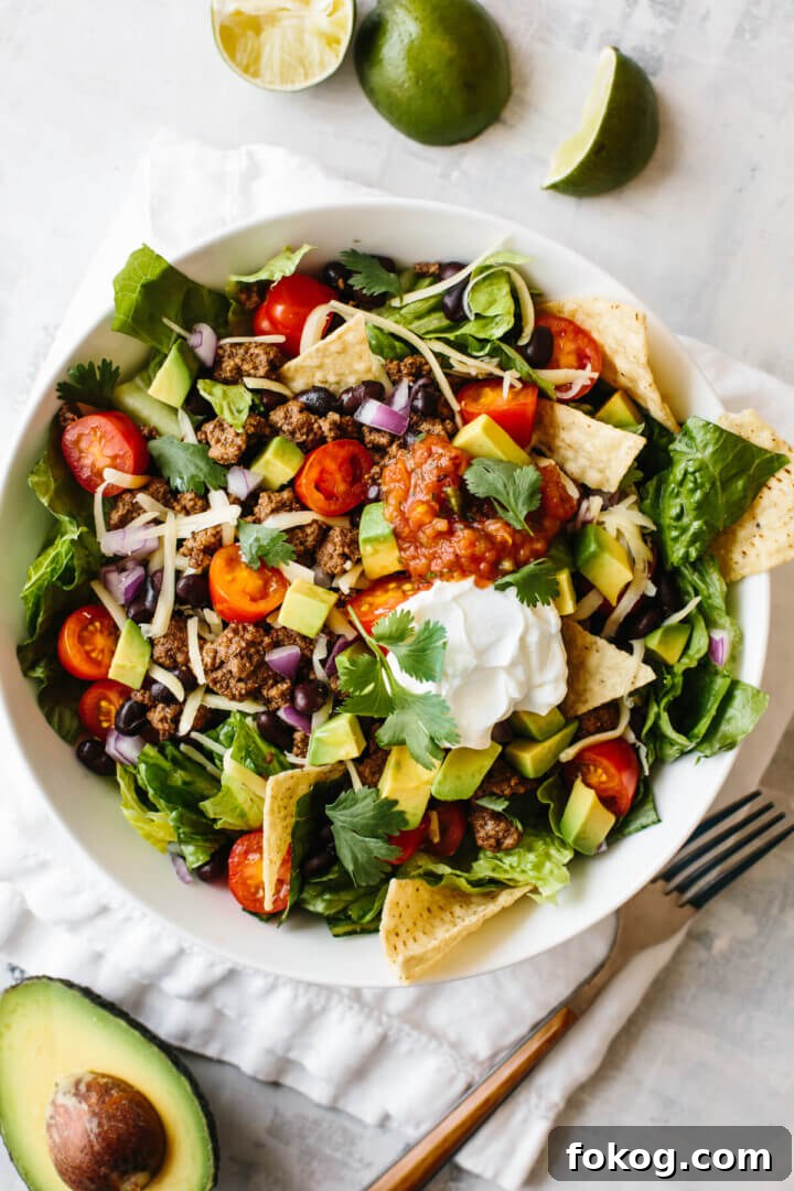 40+ Low-Carb Recipes for Weight Loss and Blood Sugar Control 9 Taco salad in a white bowl on top of a napkin, with limes and half an avocado next to the bowl.