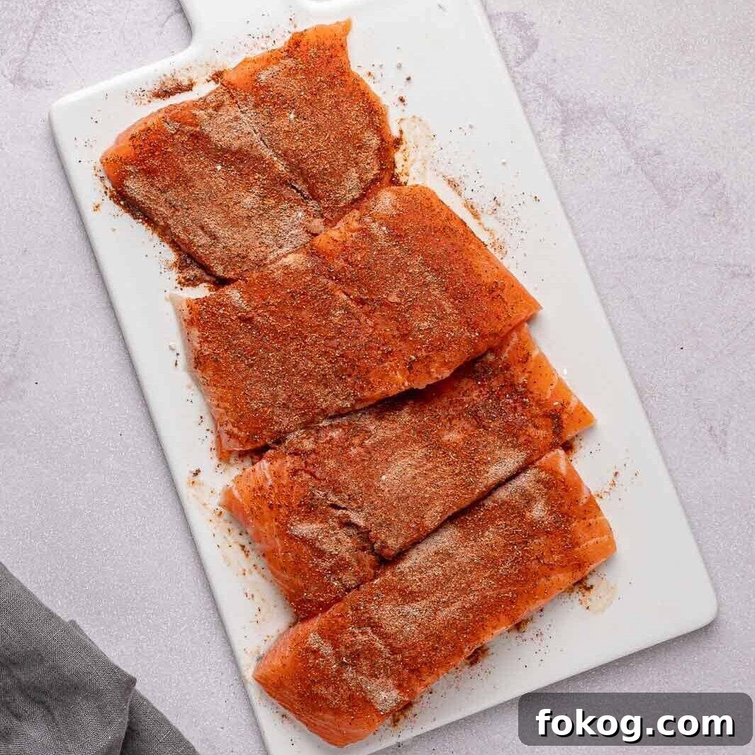 Four salmon fillets coated evenly in a red spice rub on a cutting board.