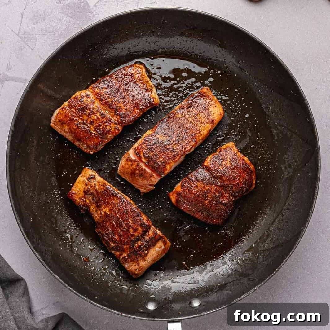 Seasoned salmon fillets searing in a hot skillet with a golden-brown crust forming.