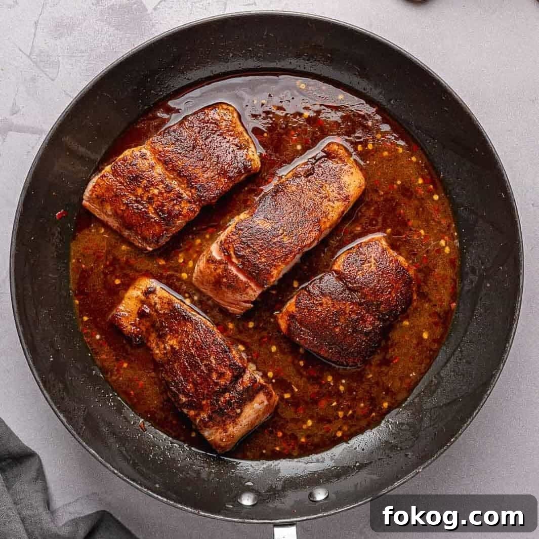 Honey garlic sauce bubbling over seared salmon in the pan.