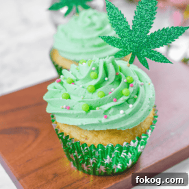A white countertop with a cutting board and a cannabis cupcake topped with green frosting