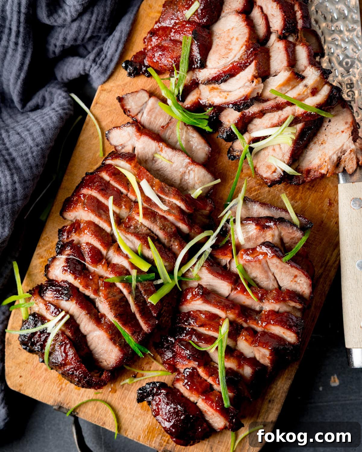 Sliced Chinese BBQ pork arranged on a wooden chopping board, garnished with thin strips of spring onion.