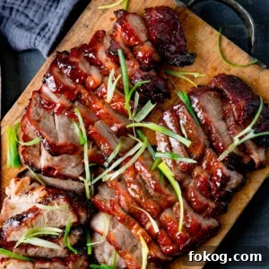 Sliced glazed char siu pork garnished with thin strips of spring onion, served on a wooden chopping board.
