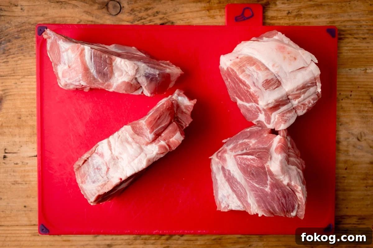 Four pork shoulder cuts placed on a red chopping board atop a wooden surface.