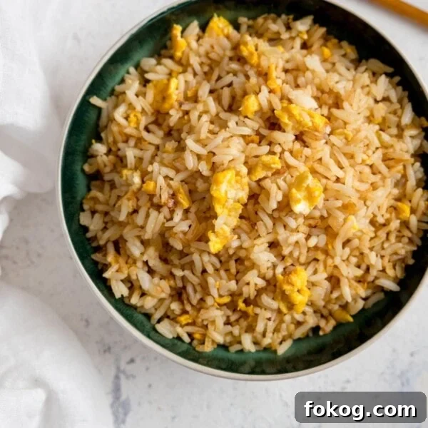 Egg fried rice on a dark bowl on a white background.