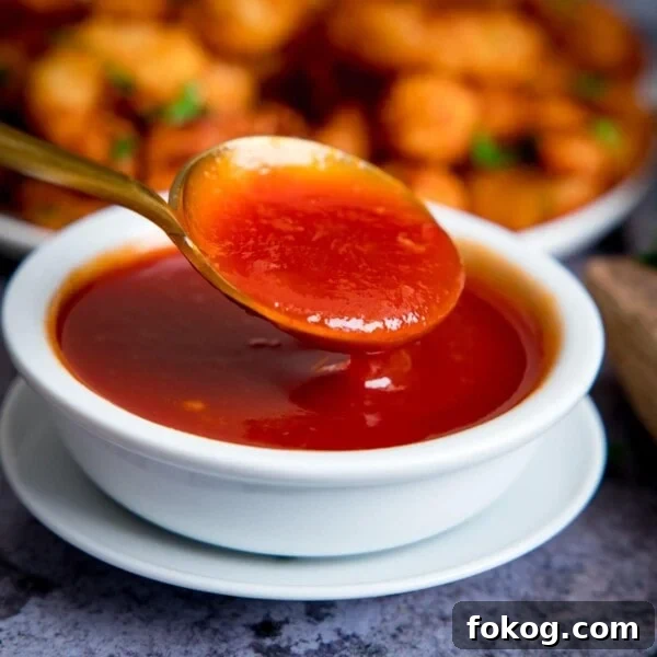 Spoonful of sweet and sour sauce being taken from a small white bowl of sauce.