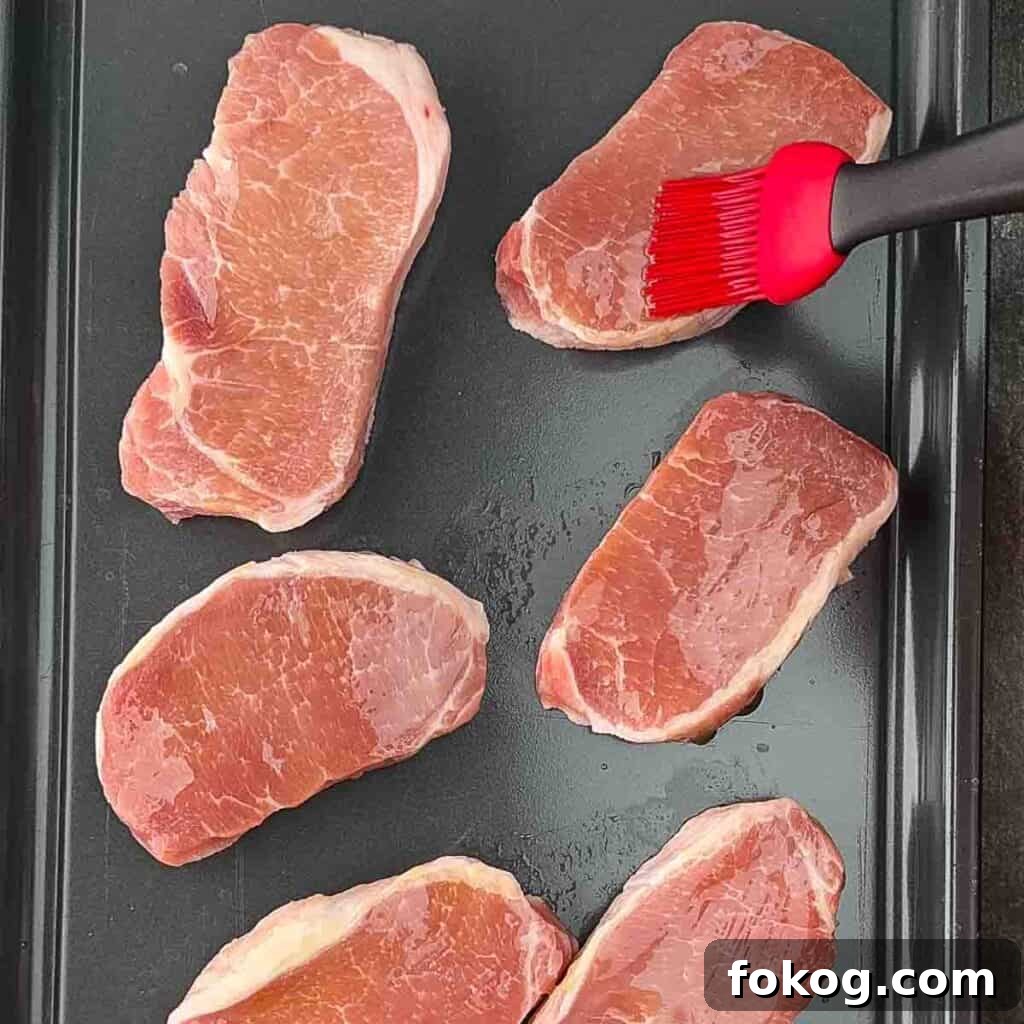 Smoked Thin-Cut Pork Chops on a Traeger Grill 4 Pork chops being brushed with olive oil on a baking sheet.