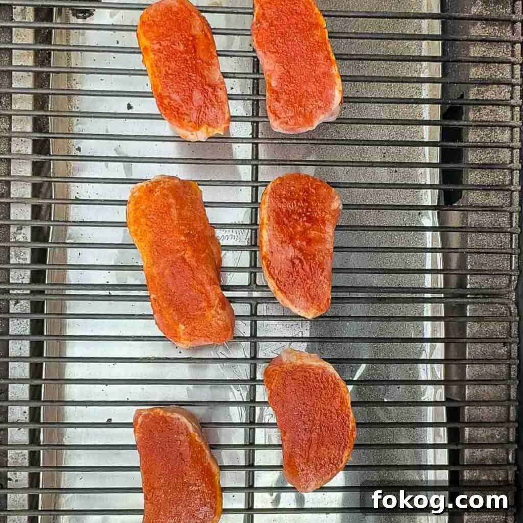 Smoked Thin-Cut Pork Chops on a Traeger Grill 6 Seasoned pork chops placed directly on the grill grates, smoking on a Traeger grill.