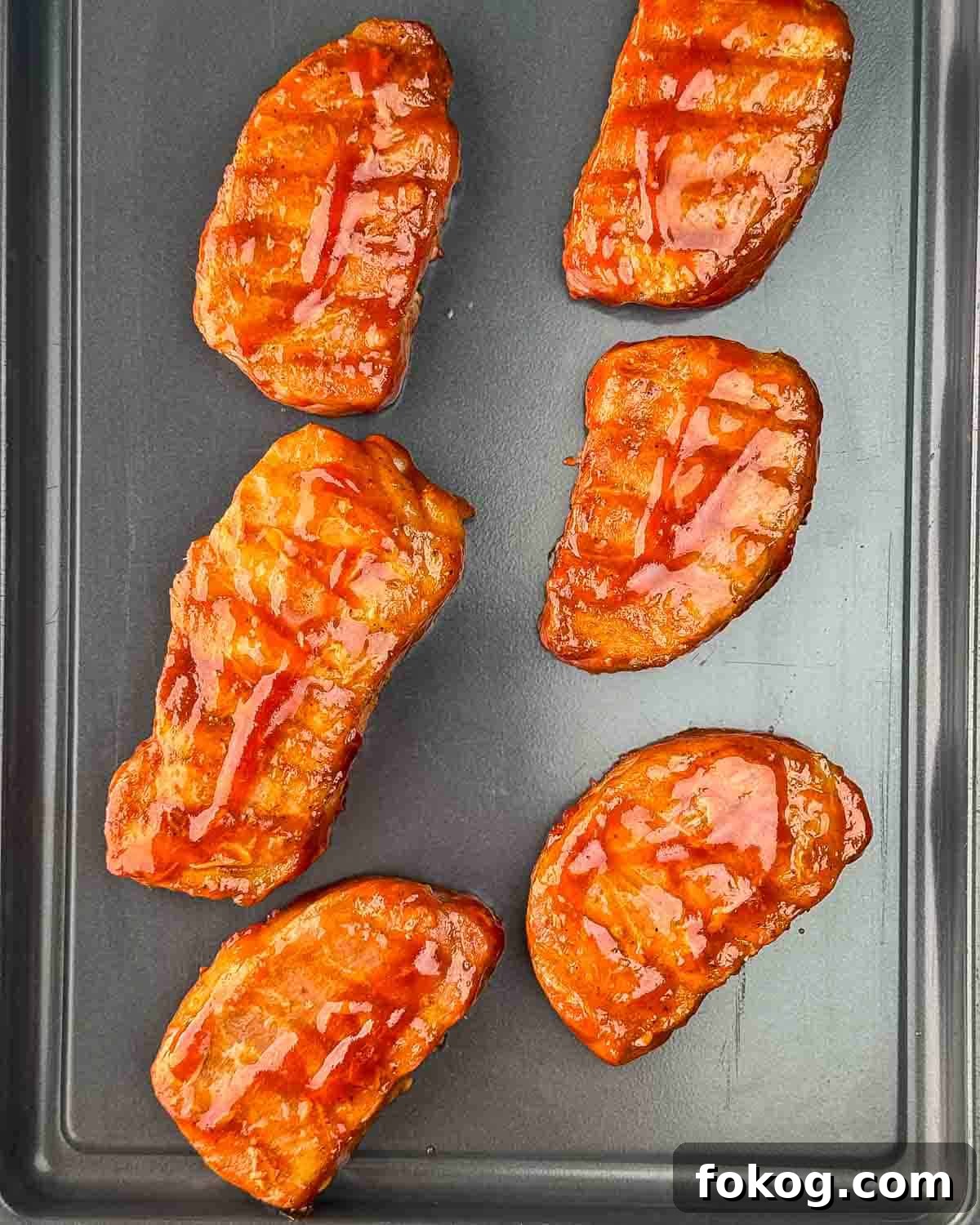 Smoked Thin-Cut Pork Chops on a Traeger Grill 9 Juicy Traeger smoked thin pork chops on a metal tray, glistening with BBQ sauce.