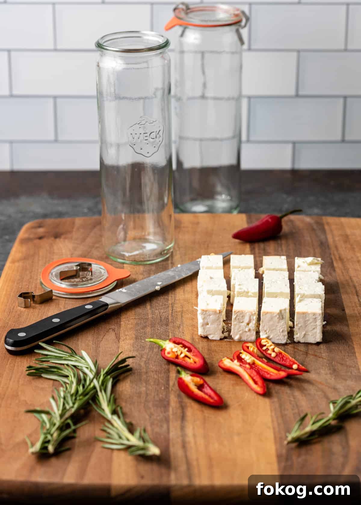 Herbed and Chili-Marinated Feta: Flavorful Appetizer Recipe 4 large wooden cutting board with cubes of fresh feta, rosemary sprigs, birdseye chili peppers and supplies for marinating cheese