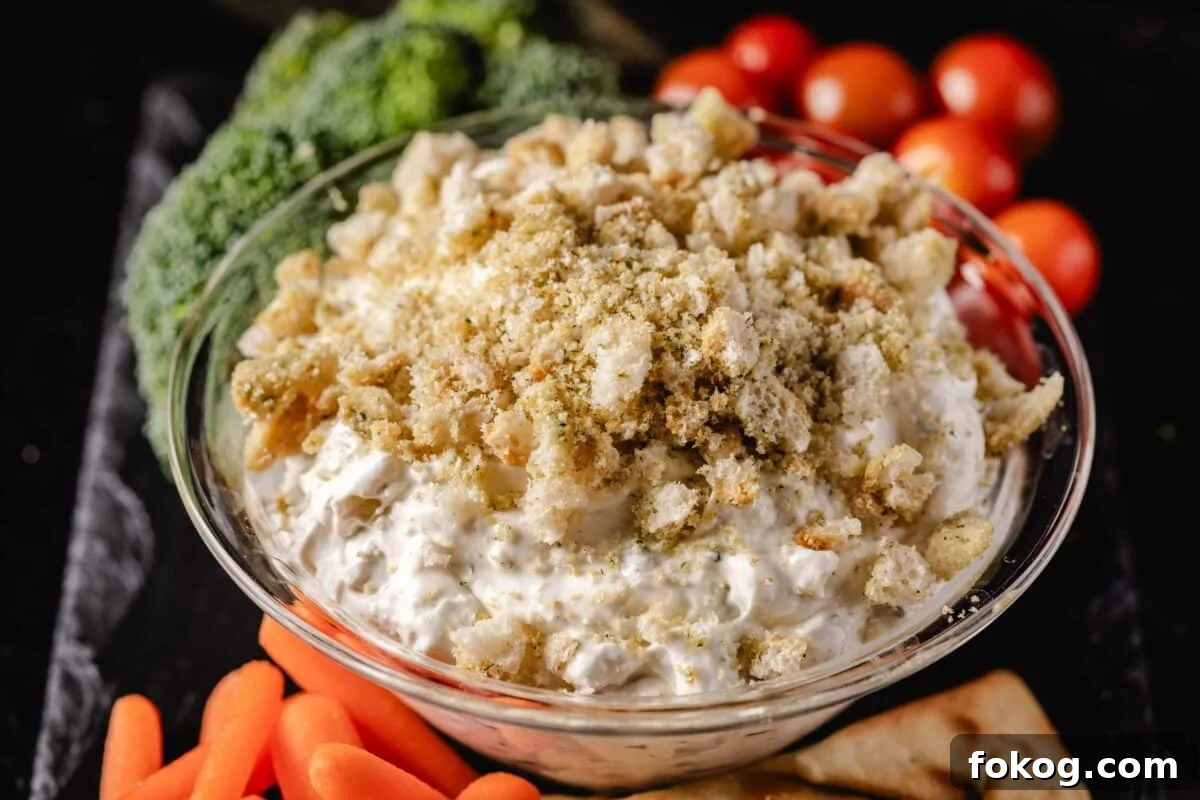 A closeup shot of a bowl of dip next to carrot sticks, broccoli, and tomatoes.
