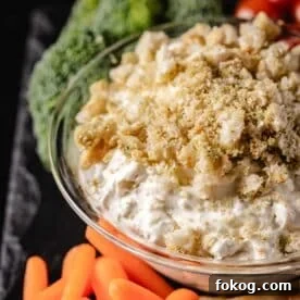 A closeup shot of a bowl of dip next to carrot sticks and broccoli.