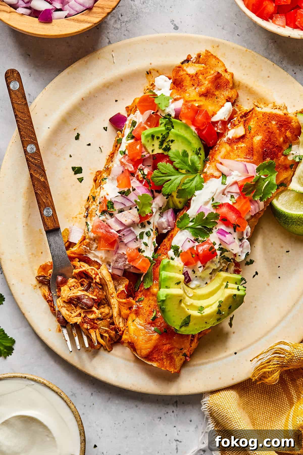 Chicken and Black Bean Enchiladas with Tangy Salsa Verde 11 enchiladas on a plate topped with avocado and salsa with a fork resting on the side.