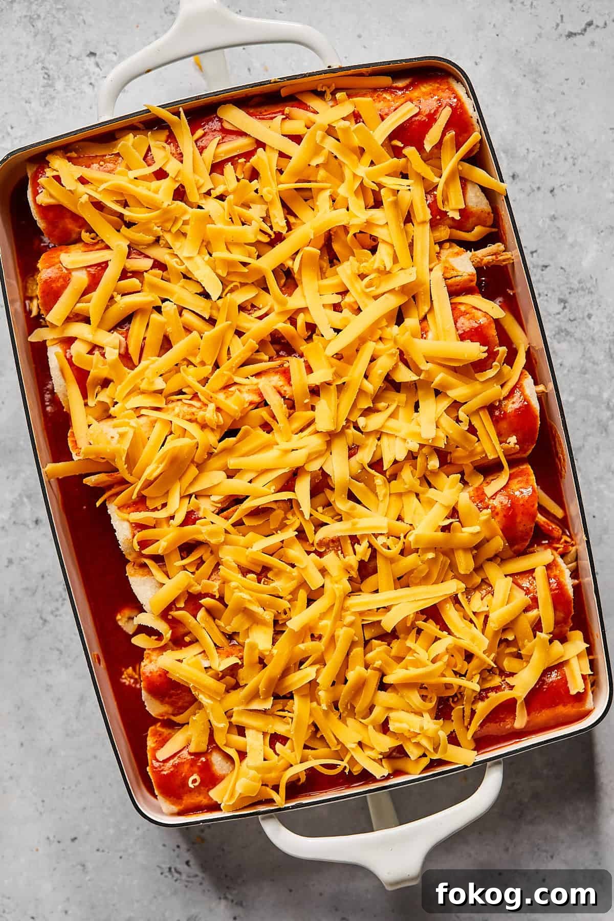 Chicken and Black Bean Enchiladas with Tangy Salsa Verde 7 a casserole dish filled with tortillas and sauce and covered in shredded cheddar cheese