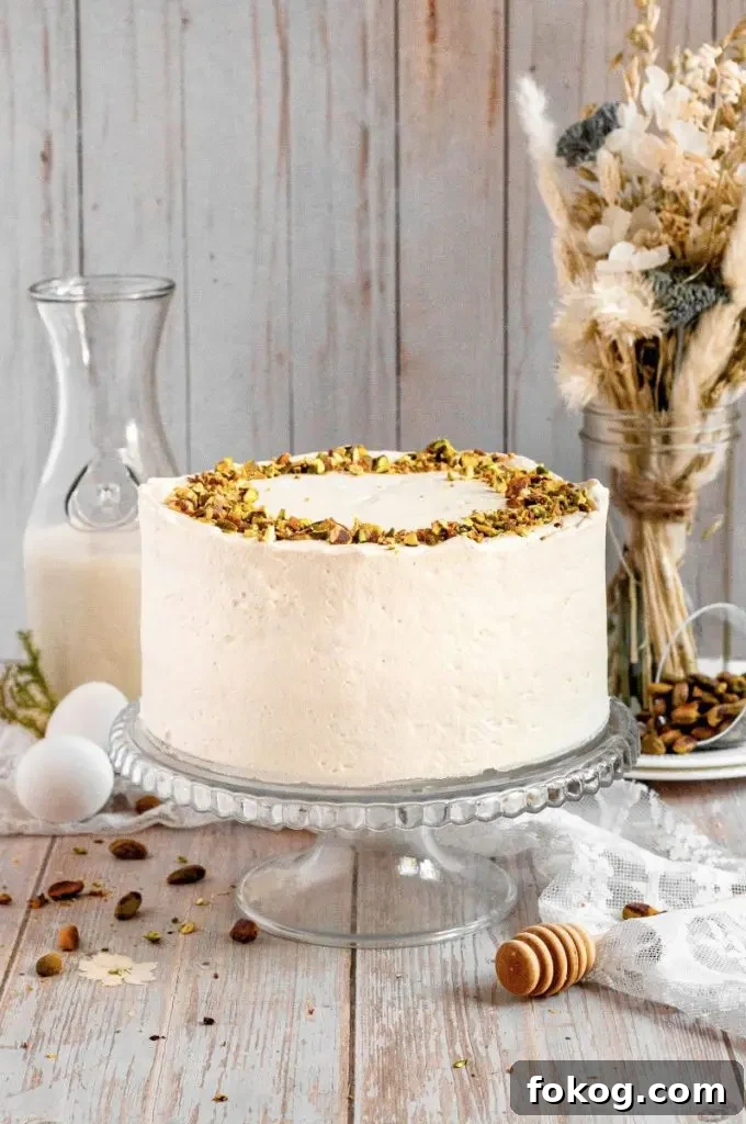 Dairy-Free Gluten-Free Pistachio Cake Recipe 4 Gluten-free pistachio cake with green cake layers, golden brown honey-roasted pistachio filling, and white whipped honey cream cheese frosting. The cake is topped with chopped pistachios.