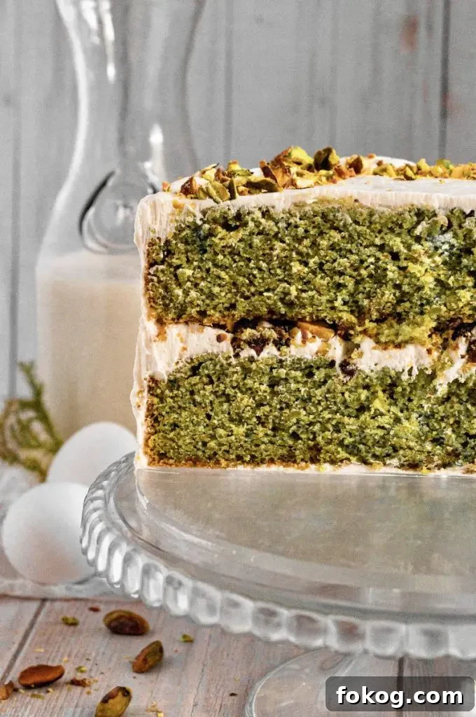 Dairy-Free Gluten-Free Pistachio Cake Recipe 5 Gluten-free pistachio cake with green cake layers, golden brown honey-roasted pistachio filling, and white whipped honey cream cheese frosting. The cake is topped with chopped pistachios.