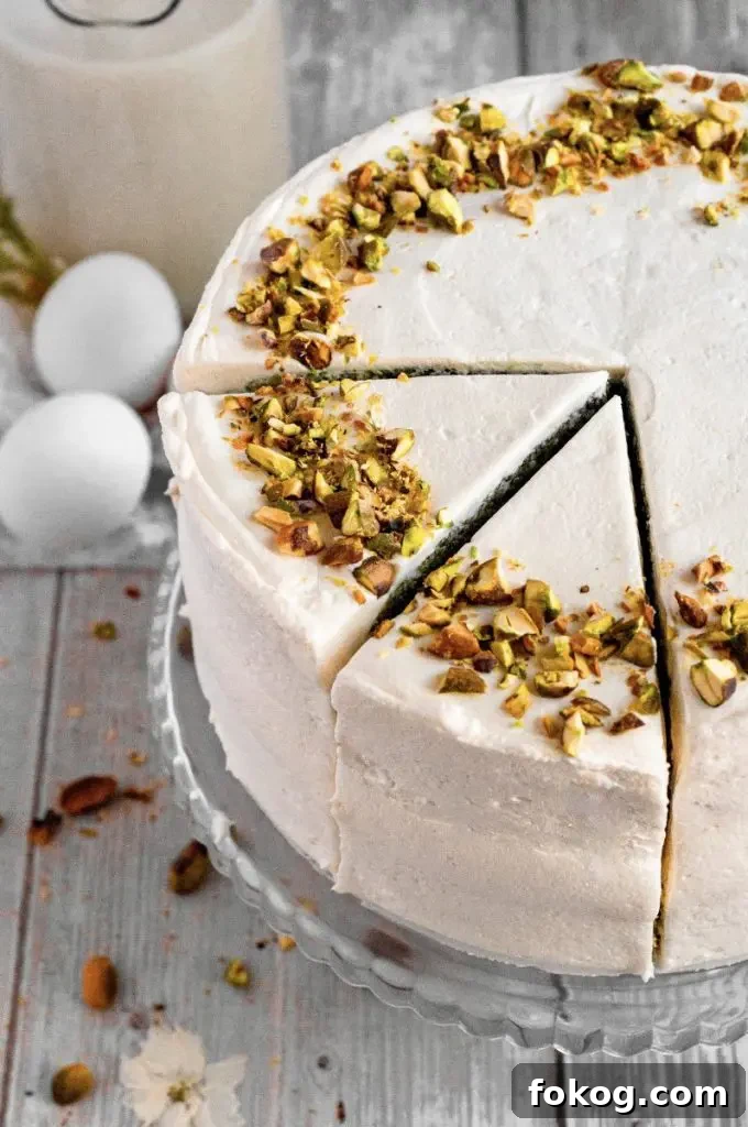 Dairy-Free Gluten-Free Pistachio Cake Recipe 6 Gluten-free pistachio cake with green cake layers, golden brown honey-roasted pistachio filling, and white whipped honey cream cheese frosting. The cake is topped with chopped pistachios.