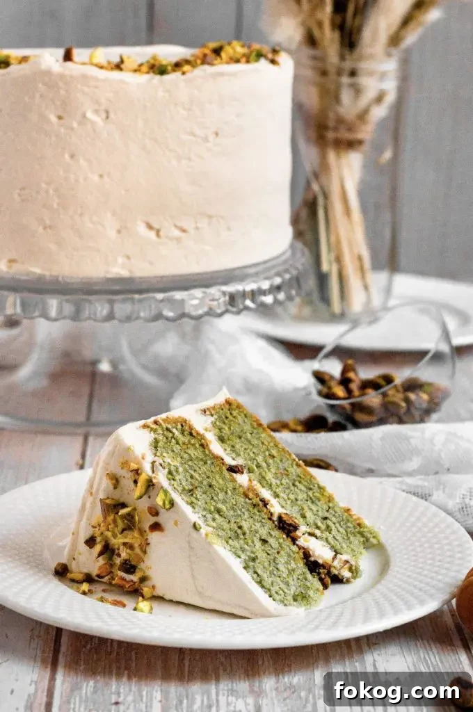 Dairy-Free Gluten-Free Pistachio Cake Recipe 7 Gluten-free pistachio cake with green cake layers, golden brown honey-roasted pistachio filling, and white whipped honey cream cheese frosting. The cake is topped with chopped pistachios.
