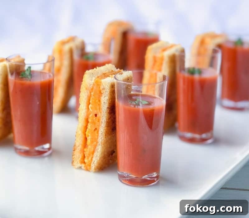 Grilled cheese sticks next to tomato soup shooter.