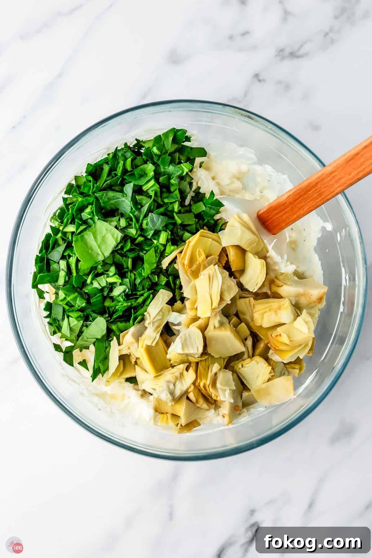 bowl of creamy dip with fresh spinach and artichoke hearts on top.