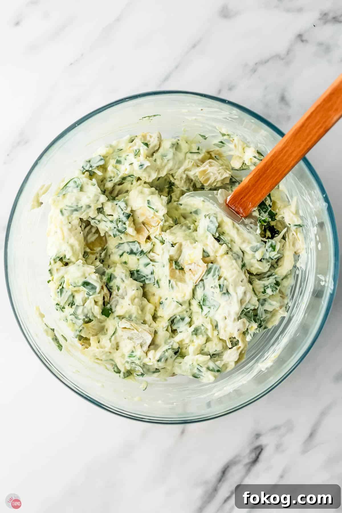 spinach artichoke dip in a clear bowl with a red spatula