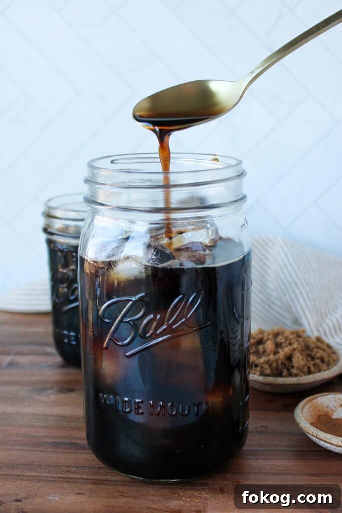 Iced Brown Sugar Latte Recipe — Creamy Cold Coffee Drink 6 Brown sugar syrup being drizzled into a mason jar full of iced coffee.