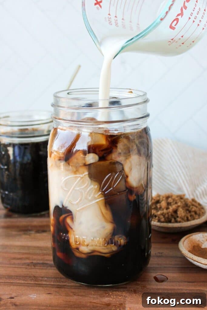 Iced Brown Sugar Latte Recipe — Creamy Cold Coffee Drink 7 A large mason jar full of coffee and brown sugar syrup with milk being poured into it.