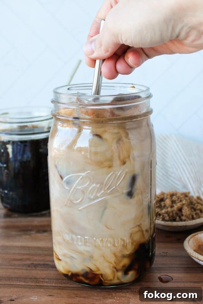Iced Brown Sugar Latte Recipe — Creamy Cold Coffee Drink 9 A large mason jar full of brown sugar coffee and ice being stirred with a stainless steel straw.