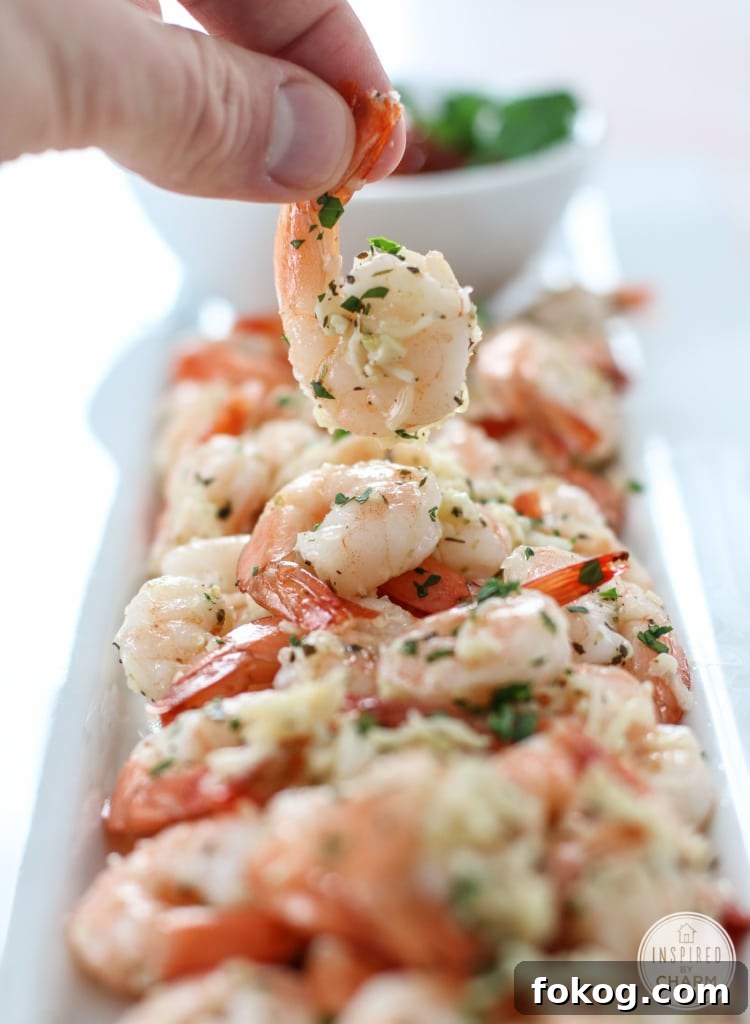 hand holding a Roasted Parmesan Garlic Shrimp over a platter of more.