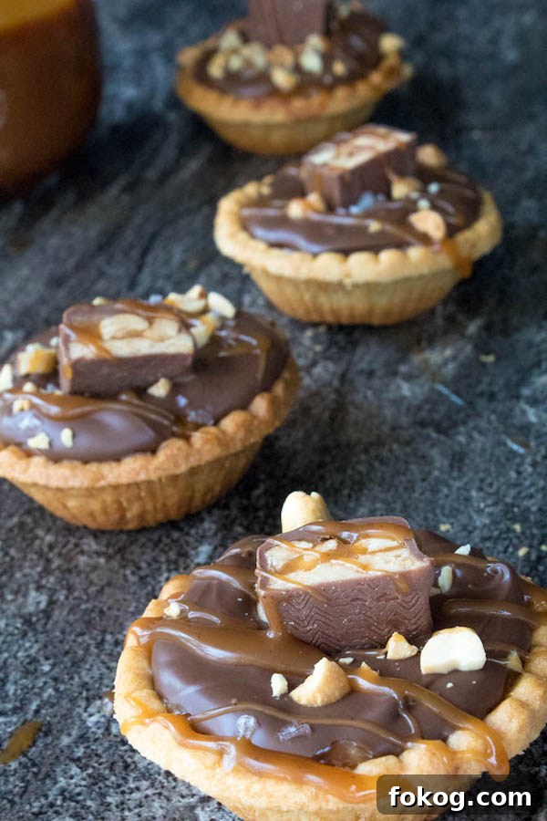 Mini Salted Caramel Snickers Tarts! Mini pre-baked tart shells with a salted caramel peanut filling and a chocolate peanut butter topping. Finish it off with chopped snickers and more peanuts, and you have the easiest/most decadent and delicious, bite-sized dessert!