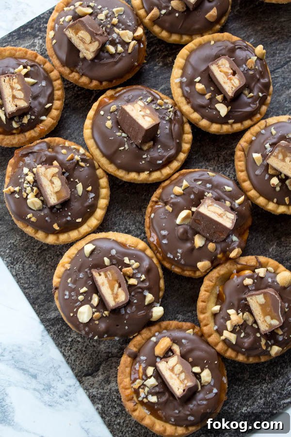 Mini Salted Caramel Snickers Tarts! Mini pre-baked tart shells with a salted caramel peanut filling and a chocolate peanut butter topping. Finish it off with chopped snickers and more peanuts, and you have the easiest/most decadent and delicious, bite-sized dessert!