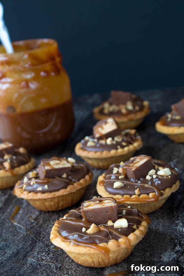 Mini Salted Caramel Snickers Tarts! Mini pre-baked tart shells with a salted caramel peanut filling and a chocolate peanut butter topping. Finish it off with chopped snickers and more peanuts, and you have the easiest/most decadent and delicious, bite-sized dessert!