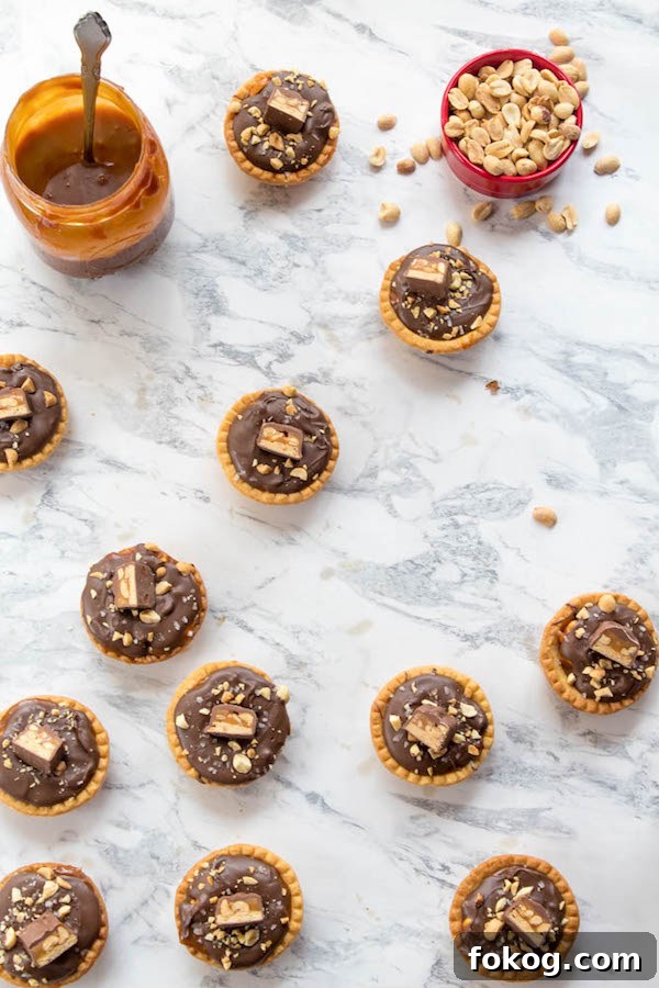 Mini Salted Caramel Snickers Tarts! Mini pre-baked tart shells with a salted caramel peanut filling and a chocolate peanut butter topping. Finish it off with chopped snickers and more peanuts, and you have the easiest/most decadent and delicious, bite-sized dessert!