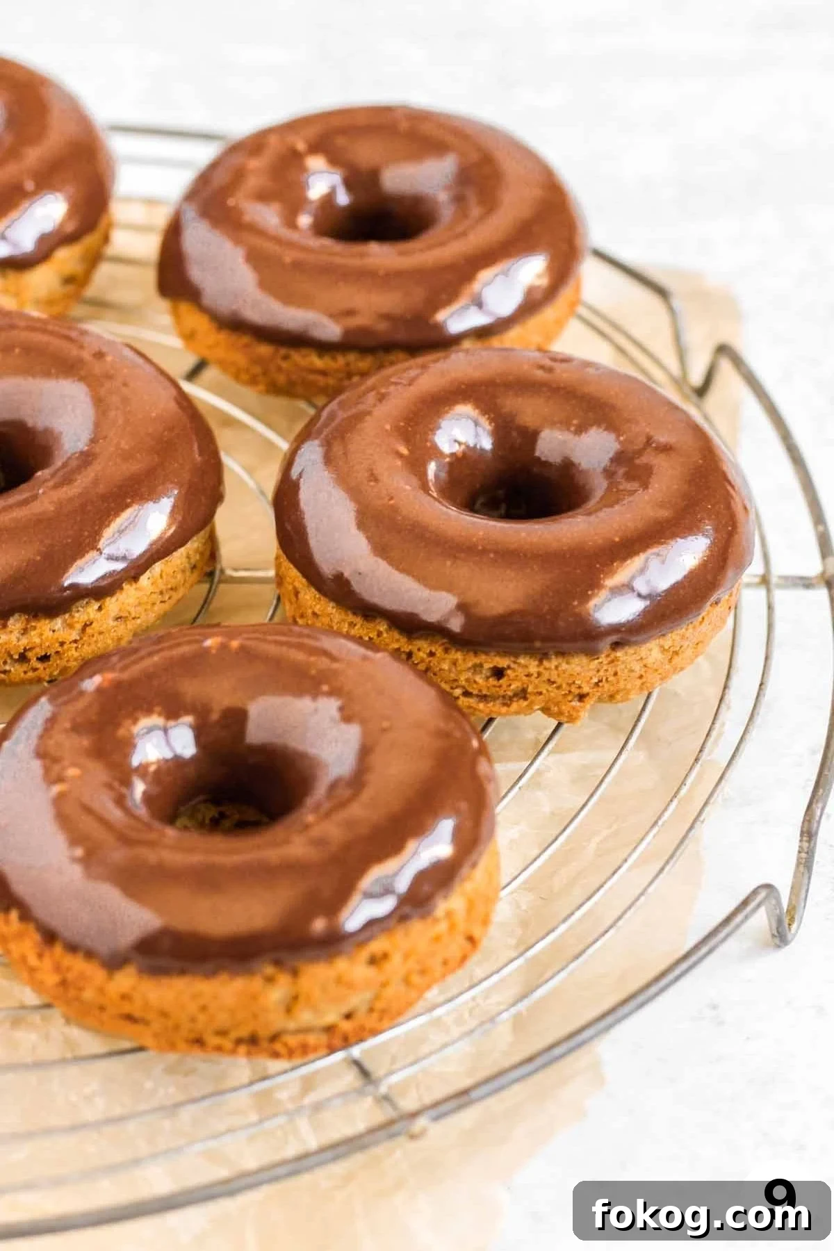 Chocolate frosted donuts on a round wire cooling rack.
