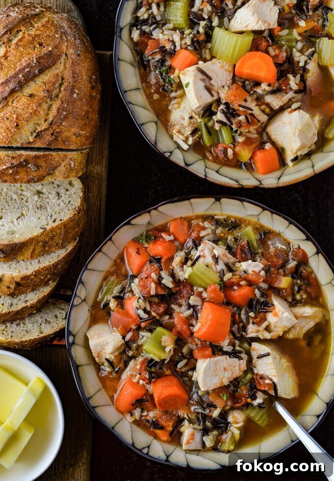 Hearty Chicken and Wild Rice Soup Recipe for Cozy Nights 2 Two bowls of wild rice chicken soup loaded with carrots, onions and celery. A sliced loaf of bread with butter sits next to the soup.