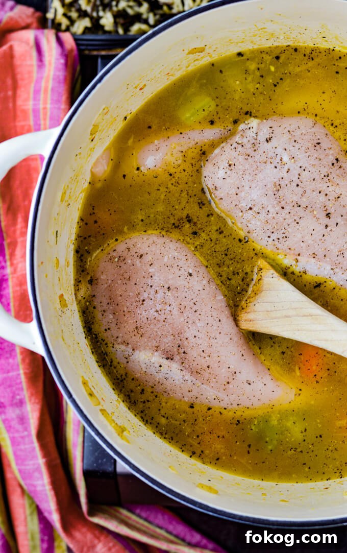 Hearty Chicken and Wild Rice Soup Recipe for Cozy Nights 5 A Dutch oven with chicken broth with raw chicken breast sitting in it.