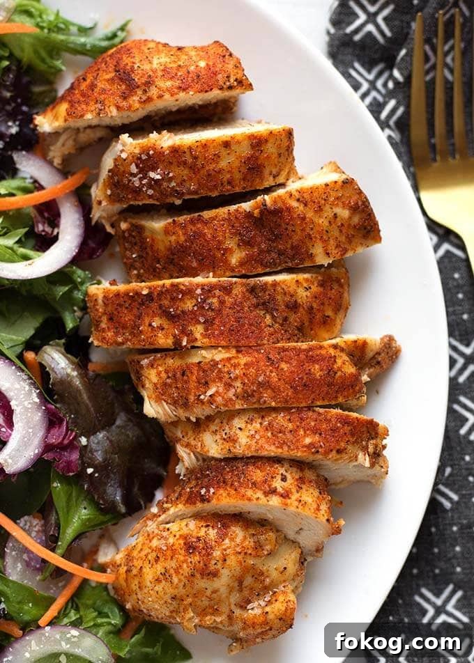 sliced chicken breast on a white plate next to a salad