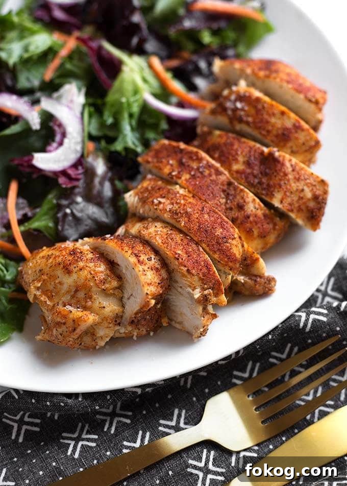 sliced chicken breast on a white plate next to a salad