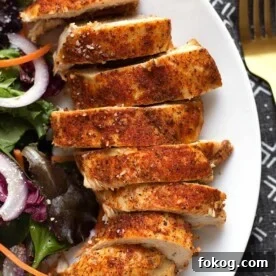 sliced chicken breast on a white plate next to a salad