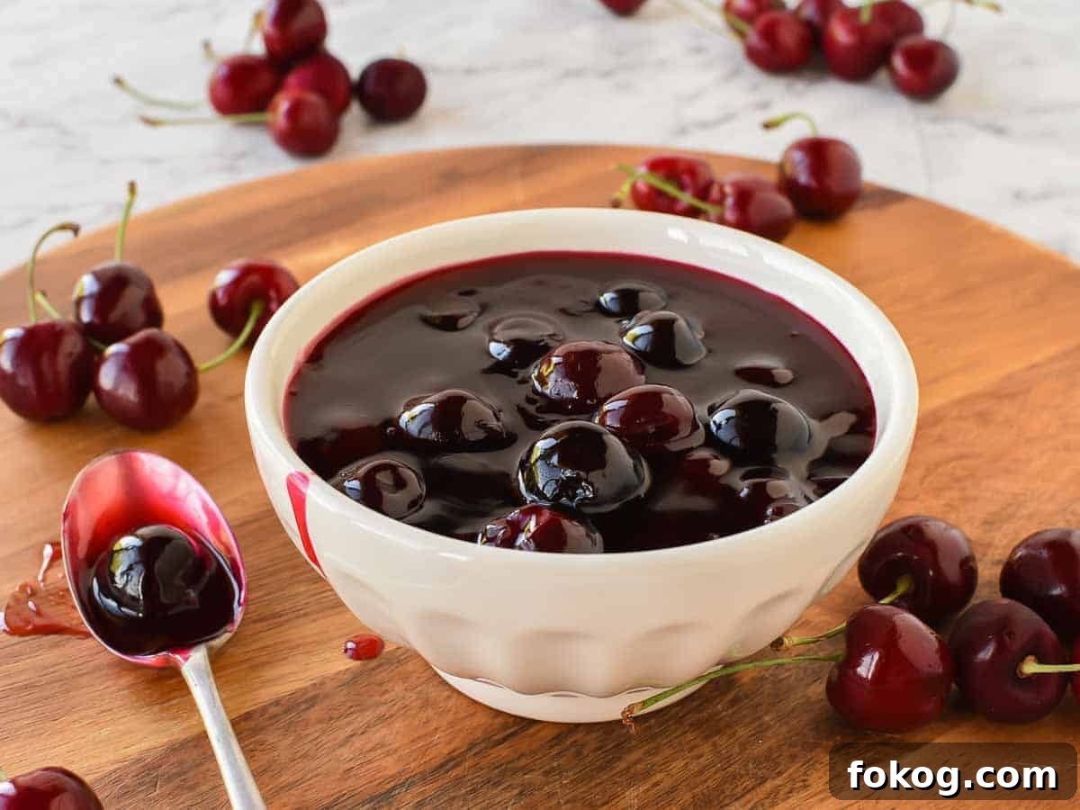 Cherry Sauce using only 5 ingredients is easy to make at home. Perfect to use for cakes, cheesecakes, ice cream, pancakes, waffles or any dessert. #cherrysauce #easy #recipe #fresh#frozen #icecream #cheesecake #sweet #best #cherry #fruitsauce #dessert Cherry sauce in white bowl with cherries scattered around, spoonful of sauce beside bowl.
