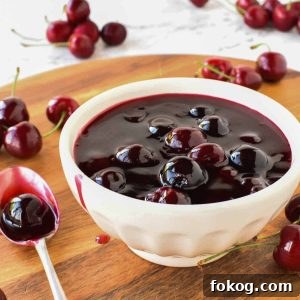 Homemade Cherry Sauce Recipe for Desserts and Toppings 2 Cherry sauce in white bowl with cherries scattered around, spoonful of sauce beside bowl